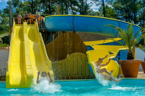 Kinder und Erwachsene rutschen auf bunten Wasserrutschen im Flower Camping Les Dunes, Pays de la Loire, Frankreich.