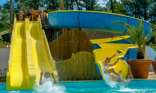 Bambini e adulti si divertono sugli scivoli d’acqua a Flower Camping Les Dunes, Pays de la Loire, Francia.