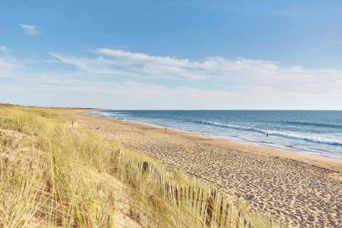Ruhiger Sandstrand von Flower Camping Les Dunes in Pays de la Loire, Frankreich mit Dünen und blauem Himmel.