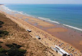 Luchtfoto van de drukke zandstrand bij Flower Camping Les Dunes in Pays de la Loire, Frankrijk, met bezoekers.
