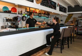 Eine Frau erhält ein Getränk an der Bar im Flower Camping Les Dunes, Pays de la Loire, Frankreich.