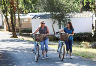 Twee vrouwen wandelen met fietsen naast stacaravans op Flower Camping Les Dunes in Pays de la Loire, Frankrijk.