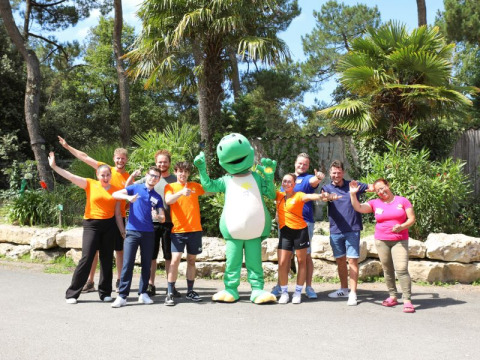 Gruppe mennesker og en grøn maskot poserer udenfor ved Flower Camping Les Dunes i Pays de la Loire, Frankrig.