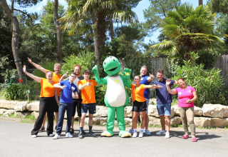 Grupo de personas y una mascota verde posando felices al aire libre en Flower Camping Les Dunes, Pays de la Loire, Francia.