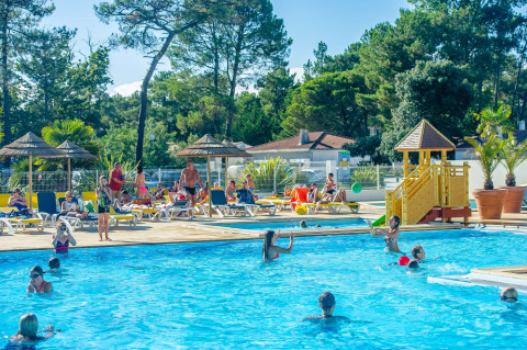Familien entspannen am Pool mit Liegen und Spielplatz im Flower Camping Les Dunes, Pays de la Loire, Frankreich.
