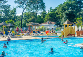 Famiglie si godono una giornata di sole in piscina con sdraio e area giochi al Flower Camping Les Dunes.