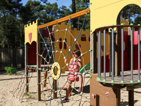 Un bambino si arrampica su una rete da arrampicata in un parco giochi a tema castello a Flower Camping Les Dunes.