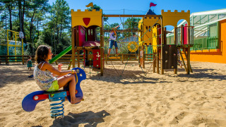 Børn leger på legeplads med sandbund og farverigt udstyr på Flower Camping Les Dunes i Pays de la Loire.