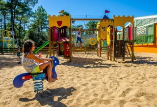 Børn leger på legeplads med sandbund og farverigt udstyr på Flower Camping Les Dunes i Pays de la Loire.