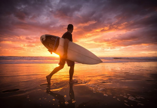 Un surfeur marche sur la plage au coucher du soleil près de Longeville-sur-Mer en Pays de la Loire, France.