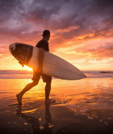 En surfer går langs stranden ved solnedgang nær Longeville-sur-Mer i Pays de la Loire, Frankrig.