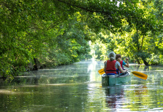 Zwei Menschen paddeln in einem Kanu auf einem ruhigen Fluss im grünen Wald bei Longeville-sur-Mer.