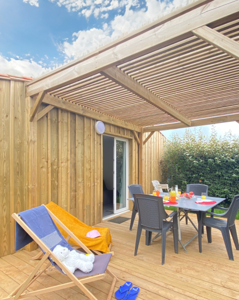 Terrazza in legno in un alloggio glamping con tavolo apparecchiato, sdraio e pergolato al sole.
