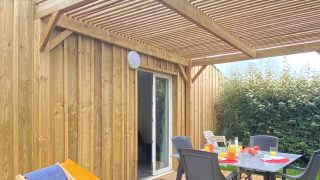 Terrazza in legno in un alloggio glamping con tavolo apparecchiato, sdraio e pergolato al sole.