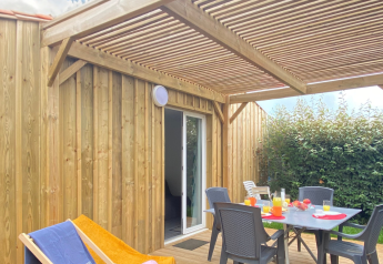Holzterrasse einer Glamping-Unterkunft mit gedecktem Tisch, Liegestuhl und sonnigem Himmel.