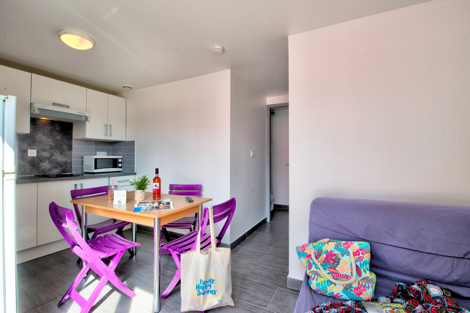 Licht glampingverblijf met moderne keuken, paarse stoelen, eettafel en een comfortabele bank.