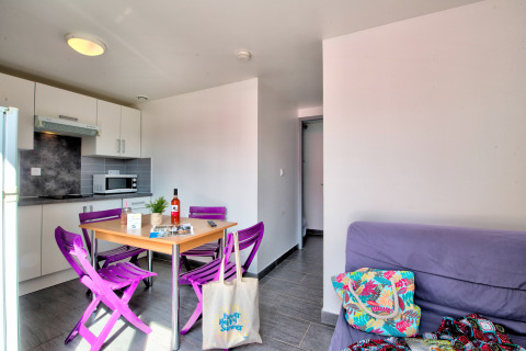 Bright glamping accommodation with modern kitchenette, purple chairs, a dining table, and a cozy sofa.