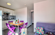 Alojamiento glamping luminoso con cocina moderna, sillas moradas, mesa de comedor y sofá acogedor.