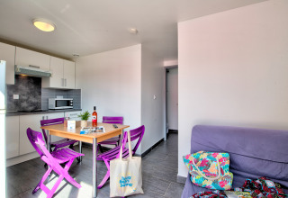 Alojamiento glamping luminoso con cocina moderna, sillas moradas, mesa de comedor y sofá acogedor.