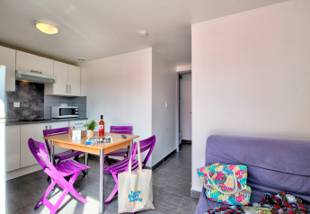 Alloggio glamping luminoso con angolo cottura moderno, sedie viola, tavolo da pranzo e divano accogliente.