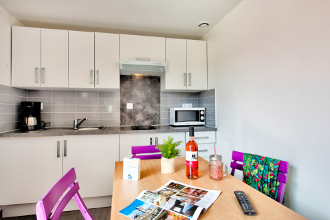 Modern glamping kitchenette with purple chairs, bottle of wine, microwave, coffee maker and bright decor.