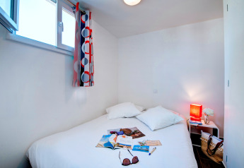 Lyst soveværelse i Huis COMFORT-hytte med dobbeltseng, åbent vindue og farverig gardin ved Flower Camping Les Ilates.