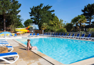 Vrouw aan het zwembad met ligzetels en waterglijbaan bij Flower Camping Port de la Chaîne in Bretagne, Frankrijk.