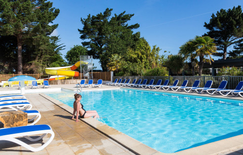 Vrouw bij buitenzwembad met ligstoelen en glijbaan in Flower Camping Port de la Chaîne in Bretagne, Frankrijk.