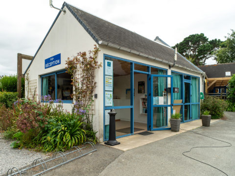 Receptie van Flower Camping Port de la Chaîne in Bretagne, Frankrijk, met blauwe kozijnen en bloemenperken.