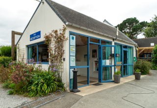 Receptie van Flower Camping Port de la Chaîne in Bretagne, Frankrijk, met blauwe kozijnen en bloemenperken.
