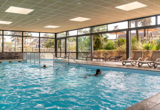 Indendørs swimmingpool med store vinduer og liggestole på Flower Camping Port de la Chaîne, Bretagne, Frankrig.