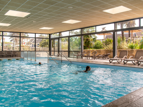Piscine intérieure avec de grandes baies vitrées et transats au Flower Camping Port de la Chaîne, Bretagne, France.