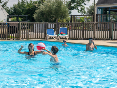 Gezin speelt en zwemt met een bal in het zwembad bij Flower Camping Port de la Chaîne, Bretagne, Frankrijk.