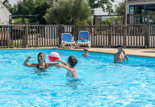 Gezin speelt en zwemt met een bal in het zwembad bij Flower Camping Port de la Chaîne, Bretagne, Frankrijk.