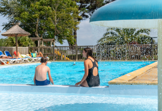 Zwei Personen entspannen sich am Pool unter einem Pilzbrunnen in einem Ferienpark in der Bretagne, Frankreich.