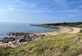 Coastal view at Flower Camping Port de la Chaîne in Brittany, France, showing rocky beach, sea and grassy dune.