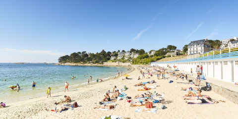 People sunbathing and swimming on a sandy beach at Flower Camping Port de la Chaîne in Brittany, France.