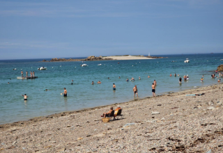 Folk bader og slapper af på en stenstrand ved Flower Camping Port de la Chaîne i Bretagne, Frankrig.