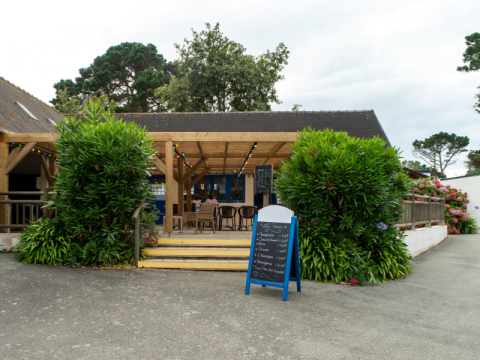 Terraza exterior con mesas, sillas y cartel de menú en Flower Camping Port de la Chaîne, en Bretaña, Francia.