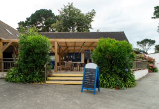 Buitenterras met tafels, stoelen en menu bord bij Flower Camping Port de la Chaîne in Bretagne, Frankrijk.