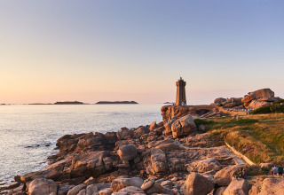 Sunset along the coast near Pleubian, Brittany, France, featuring a lighthouse and rocky shoreline by the sea.