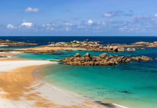 Smuk udsigt over stranden, turkisblå vand og klippeøer ved Flower Camping Port de la Chaîne, Bretagne.