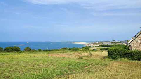 Vista costera cerca de Pleubian en Bretaña, Francia, con campos verdes, mar azul y casas al fondo.
