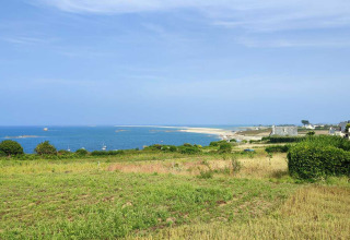 Vista costiera vicino a Pleubian, Bretagna, Francia, con campi verdi, mare blu e case sullo sfondo.