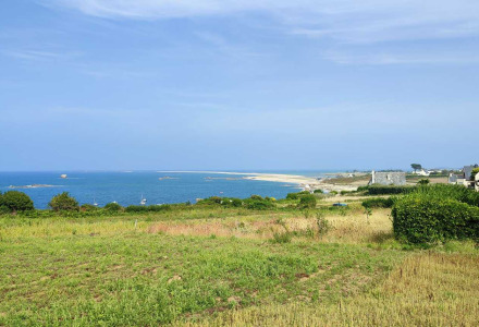 Vue côtière autour de Pleubian en Bretagne, France, avec champs, mer bleue et maisons en arrière-plan.