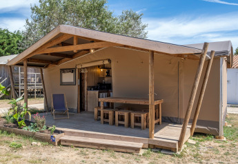 Safari-Zelt bei Ecolodge cabine Cotton CONFORT mit Holzterrasse, Garten und Sitzgelegenheiten draußen.