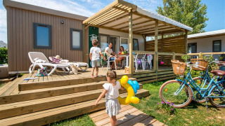Gezin beleeft plezier op het terras van Homeflower PREMIUM lodge met kinderen en fietsen in de zon.