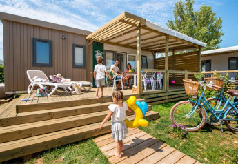 Gezin beleeft plezier op het terras van Homeflower PREMIUM lodge met kinderen en fietsen in de zon.