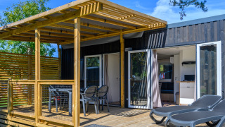 Alojamiento glamping con terraza de madera, tumbonas y comedor cubierto bajo cielo azul y árboles verdes.