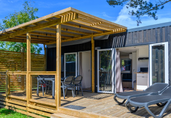 Glampingaccommodatie met terras in hout, ligstoelen en een overdekte eethoek bij zonnig weer.